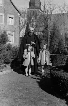 Kapuzinerpater Mainolf mit den Kindern von Günter Rhode, Nottuln - im Hintergrund die St. Martinus-Kirche, undatiert, Ende 1940er Jahre?