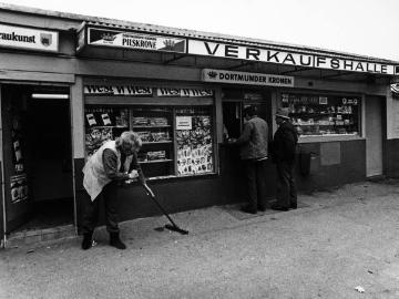 Fegen vor der Trinkhalle. Dortmund [?]. Undatiert, 1980er Jahre. 