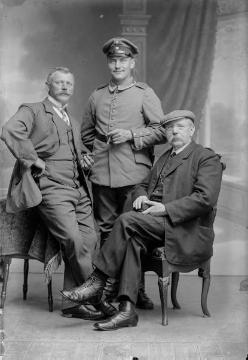 Fotograf und Ladenbesitzer Johann Hermann Jäger (1845-1920) mit zwei Herren (stehend). Atelier Jäger, Harsewinkel, um 1914.
