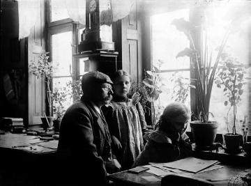 Fotograf und Ladenbesitzer Johann Hermann Jäger in seinem Büro - neben ihm die Töchter Änne (*1896) und Gertrud (*1899) aus seiner zweiten Ehe mit Gertrud Jäger, die jüngsten seiner neun Kinder. Harsewinkel, Kirchplatz 179. Undatiert, um 1905.