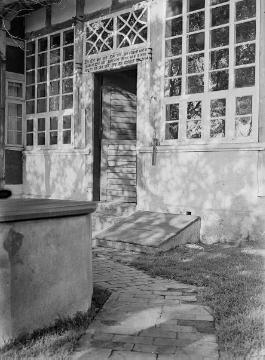 Sproßenfensterfassade eines Fachwerkhauses und Eingangstür mit Inschrift. Vorn: Brunnen und Kellerklappe. Vermutlich Raum Enger. Ohne Angaben, undatiert, 1940er Jahre?