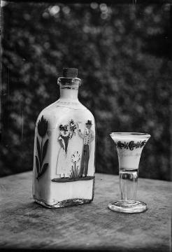 Bäuerlicher Hausrat: Karaffe mit Darstellung eines Hochzeitspaares [?] und Trinkglas. Ohne Angaben, undatiert.