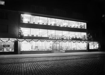 Möbel Wiek, Hamm, Weihnachten1960 - Geschäftsgebäude in der Wilhelmstraße 22-23. Links: Schnellreinigung Schulte, rechts: Puppenklinik [Wilhemstraße mit Kopfsteinpflaster].