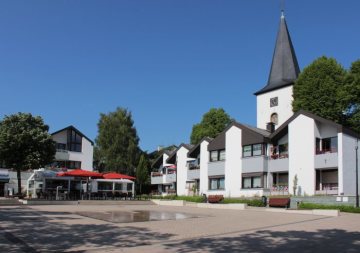 Pankratius-Platz mit Wohanlage und St. Pankratius-Kirche in Möhnsee-Körbecke, 2019.