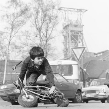 Junge mit Fahrrad auf dem Parkplatz am Werkstor von Zeche Graf Moltke, Gladbeck, 1980.