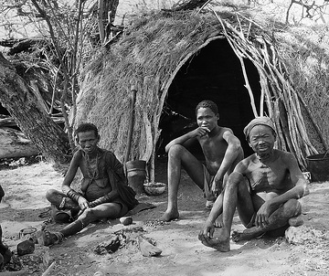 Angehörige der Volksgruppe der San (oder auch Basarwa) vor einer traditionellen Hütte [Originaltitel: Buschmannsfamilie vor ihrer zweigedeckten Hütte]