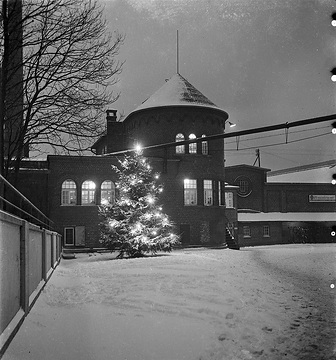 Industrieunternehmen mit elektrisch beleuchtetem Weihnachtsbaum; Banner rechts am Gebäude: Hakenkreuz im Zahnrad (Deutsche Arbeitsfront), Aufschrift: "Wir marschieren mit!", undatiert, zwischen 1934 und 1938.