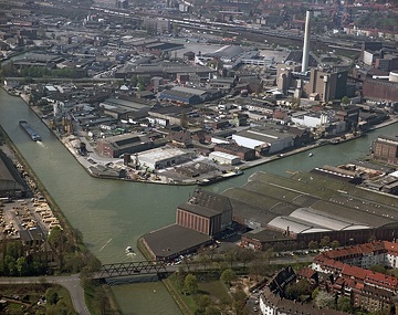 Münster, Hafen: Kanalhafen, Dortmund-Ems-Kanal, Kohle-Heizkraftwerk (errichtet 1977, 2005 auf Gas umgestellt), Osmo-Hallen; oberer Bildrand: Bahntrasse und Hauptbahnhof