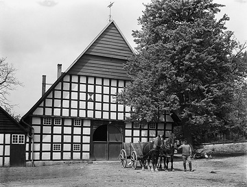 Torseitige Ansicht eines Fachwerkbauernhauses mit Pferdegespann