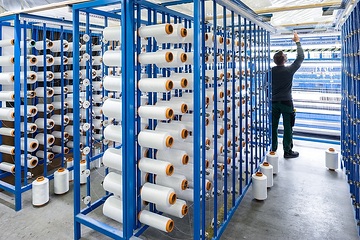 Saerbeck, Saertex GmbH & Co. KG: Die Firma produziert textile multiaxiale Gelege aus Glas-, Carbon- und Aramid-Fasern, diese dienen als Verbundstoffe im Leichtbau für Windenergie, Luft- und Schifffahrt, die Automobil- und Bauindustrie. Blick in die Produktion, von den Glasfaserspulen aus dem Gatter wird das Garn zur Nähwirkstelle geführt.