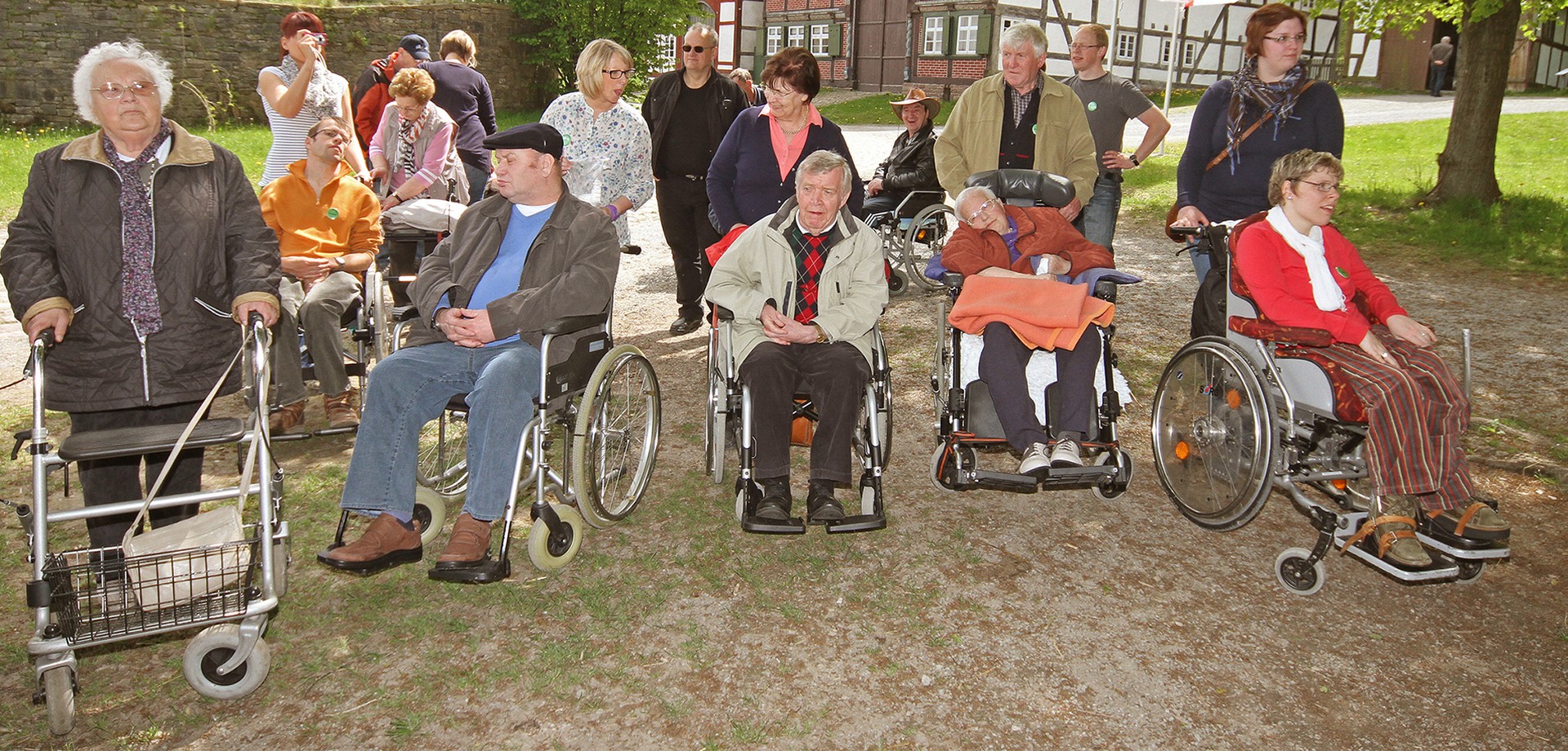 Eine Gruppe von 18 erwachsenen Personen. Einige sind schon etwas älter. Sie benutzen eine Gehhilfe oder sitzen im Rollstuhl.