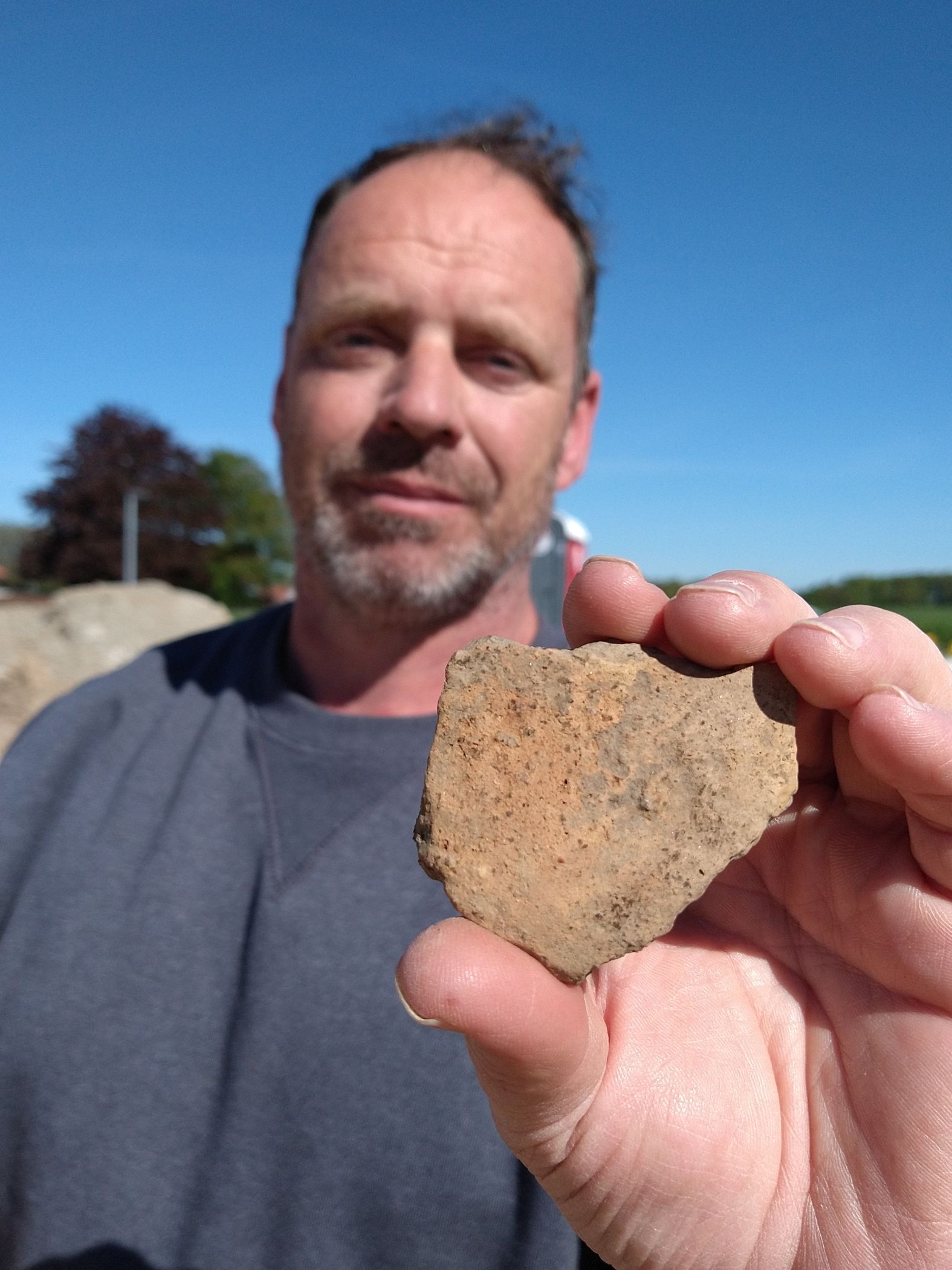 Grabungsleiter Philipp Bockelbrink zeigt eine über 2.000 Jahre alte Keramikscherbe. In solchen Gefäßen lagerten die Siedler damals ihre Lebensmittelvorräte.<br>Foto: LWL/S. Spiong