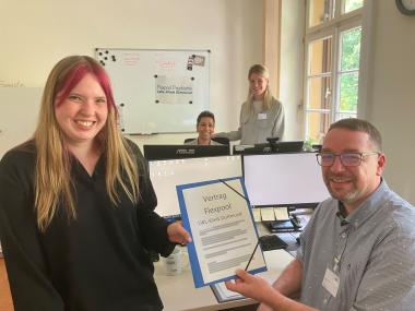 Larissa Börner (l.) hat gerade ihren Vertrag unterschrieben und bekommt ihn von Flexpool-Leiter Gregor Urbaniok überreicht. Am hinteren Schreibtisch sieht man Sony Neduvakkattu-Wardenbach und Julia Brosch vom Flexpool-Team.<br>Foto: LWL/Herstell