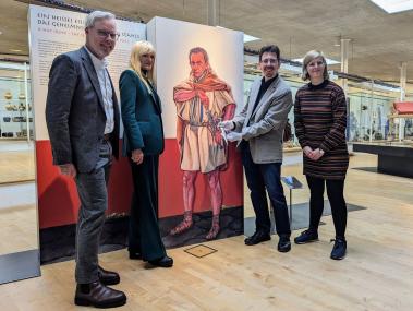 Museumsleiter Dr. Josef Mühlenbrock, Kulturdezernentin Dr. Barbara Rüschoff-Parzinger, Dr. Ulrich Lehmann von der LWL-Archäologie für Westfalen und Lisa Stratmann, Leiterin der Museumspädagogik, vor der extra für "Ein heißes Eisen! Römische Schmiedekunst" neu geschaffenen Illustration des britischen Künstlers Graham Sumner.<br>Foto: LWL/J. Großekathöfer