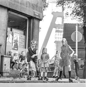 Spielende Kinder auf Rollschuhen, im Hintergrund der Förderturm von Zeche Mont Cenis in Herne-Sodingen, um 1970.<br>Foto: LWL/Orwat