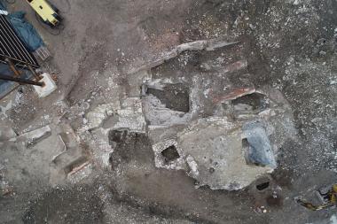 Drohnenaufnahme des aktuellen Grabungsareals. Die rechteckigen und quadratischen Eintiefungen in dem Felsen stellen die Keller dar, über denen einst die Gebäude standen. Ein quadratischer Schacht in der Bildmitte und der runde, in den Fels eingetiefte Schacht unten rechts, vermutlich ein Brunnen, sind deutlich zu erkennen.<br>Foto: Denkmal3D/H. Tausendfreund