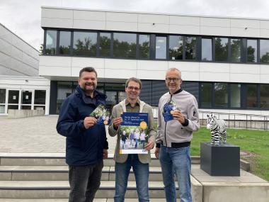 Vor dem Forschungsneubau, ZEBRA genannt und mit dem kleinen Zebra rechts  erkennbar markiert, präsentieren (v. li.) der Kaufmännische Direktor Dr. Daniel Napieralski-Rahn, der Ärztliche Direktor Prof. Dr. Dr. Martin Holtmann und Pflegedirektor Thomas Linnemann Plakate und Flyer für den "Tag der offenen Tür" am Samstag (27.9.).<br>Bild: LWL