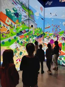 Am 2.11. stellen die Kinder des diesjährigen Herbstferienprogramms gemeinsam mit den Künstler:innen Büsra Inam und Thomas Köller von der Jugendkunstschule Herne die Ergebnisse ihres Kunstprojektes vor. Hier vor dem überdimensionalen Wimmelbild zum Thema Essen.&lt;br&gt;Foto: Jugendkunstschule Herne 