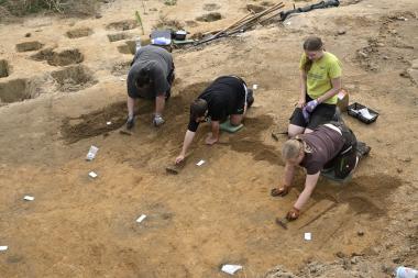 Das Grabungsteam legt die Spuren der Hauspfosten frei, die sich als dunkle Verfärbungen im gelben Lehm abzeichnen.<br>Foto: LWL/A. Koch