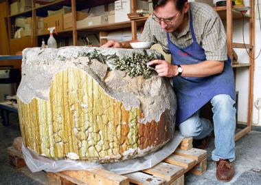 LWL-Restaurator Sebastian Pechtold legt die Oberfläche der grünlichen Glasmasse in dem großen, mehr als eineinhalb Tonnen schweren Schmelztiegel frei. </br>Foto: LWL/Egbert</br>