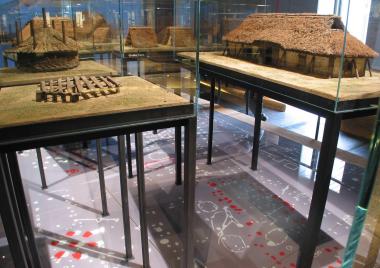 Auf dem Boden der Plan der Archäologen, in Augenhöhe die Rekonstruktionen - und so groß, dass man hindurchlaufen kann, durch das Modell der 1200 Jahre alten Siedlung in Warendorf.<br>Foto: H. Menne/LWL</br>