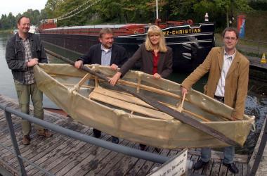 Die Museumsleiter Herbert Niewerth (2. v. l) vom Alten Schiffshebewerk Henrichenburg)  und Dr. Barbara Rüschoff-Thale (3. v. l.) vom Westfälischen Museum für Archäologie stellen das Steinzeitboot vor, das die Kinder in den Herbstferien bauen. <br>Foto:LWL/Schilp</br>