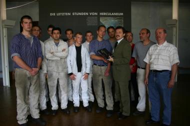 Museumschef Rudolf Aßkamp (4.v.r.) übergibt dem 10.000 Besucher Thomas Weichert einen Katalog der Herculaneum-Ausstellung.<br>Foto: LWL<br />