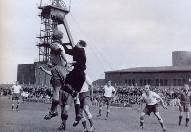 Fußball im Schatten des Förderturms: Spiel des SV Sodingen auf seiner Glück-Auf-Kampfbahn an der Zeche Mont-Cenis in Herne Anfang 1950er Jahre. <br>Foto: Ausstellung Fußballregion Ruhrgebiet<br />