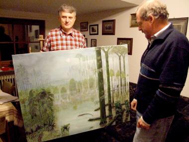 Hobbymaler und ehrenamtlicher Museumsmitarbeiter Wolfgang Sippel (l.) übergibt ein Bild von Ibbenbüren im Karbonzeitalter an Dr. Lothar Schöllmann vom Westfälischen Museum für Naturkunde. <br>Foto: LWL/Knoche<br />