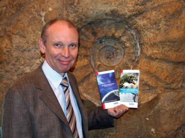 Museumsdirektor Dr. Alfred Hendricks präsentiert vor dem Riesenammoniten stehend die neue Informationsbroschüre des LWL-Museums für Naturkunde. Foto: LWL/Fialla
