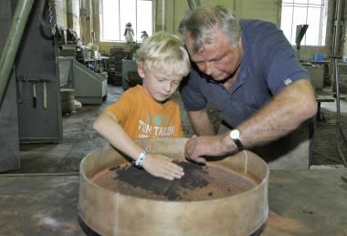 Karl Nießen zeigt Kindern in der Schaugießerei der Henrichshütte die Kunst des Formens und Gießens.<br >Foto: LWL<br />