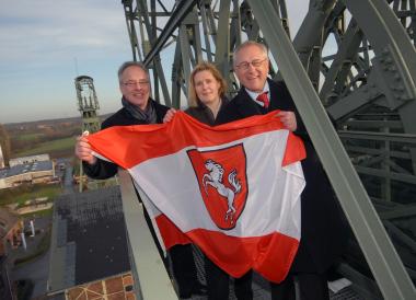 Flagge zeigen: LWL-Direktor Dr. Wolfgang Kirsch (v.r.), Standortleiterin Dr. Ulrike Gilhaus und Museumsdirektor Dirk Zache mit der Westfalen-Flagge auf dem Fördergerüst der Zeche Zollern. <br>Foto: LWL/Appelhans<br />