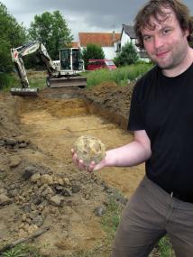 Der studentische Volontär Andreas Knäpper hält den schweren Fund: eine gusseiserne Kanonenkugel, die auf dem Gelände der geplanten Wulf-Hefe-Spange freigelegt wurde. <br>Foto: LWL/Michael Baales<br />