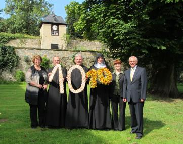 Für Leib und Seele: Mit je einer Zehn aus Brot und Blumen gratulieren Bruder Antonius Fach und Pater Werner Vullhorst OSB und Schwester Andrea Grabl OSB LWL-Direktor Dr. Wolfgang Kirsch, Museumsdirektorin Dr. Julia Hallenkamp-Lumpe und Klostermarkt-Organisatorin Marianne Rosar zum 10. Jubiläum des Dalheimer Klostermarkts. Die Zehner stammen aus den Werkstätten der beiden Klöster. Ausführliche Bildzeile im unteren Teil der Pressemeldung. <br>Foto: LWL /Tillmann<br />