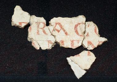 Das Dracofragment,ebenfalls nach Aachen entliehen,ist eines von vielen Wandputzfragmenten aus karolingischer Zeit,die 1964 bei Ausgrabungen auf dem Paderborner Pfalzareal gefunden wurden.Die Fragmente verweisen auf ein farbiges,eindrucksvolles Raumbild der Königspfalz und der frühen Kirchbauten. Ob das Wort Draco ein fränkischer Eigenname ist oder ob es sich um eine Anspielung auf den Drachen als Sinnbild des Bösen, das von Karl dem Großen besiegt worden ist, handelt, bleibt unklar.<br>Foto: LWL 