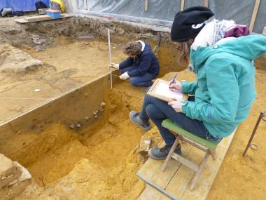 Eine der zahlreichen Gruben, die sich als dunkle Verfärbungen im Boden abzeichnen, werden von den Grabungshelfern und Archäologen dokumentiert.<br>Foto: LWL/Tremmel