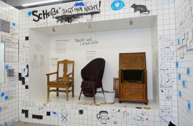 Ein Blick in die Ausstellung zeigt eine Auswahl der Toilettenstühle des LWL-Freilichtmuseums Detmold. An die Wände sind verschiedene Formen und Typen des sogenannten Nacht- und Leibstuhls gezeichnet.<br>Foto: LWL