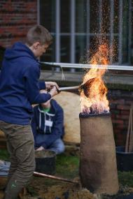 : Schüler der Heinrich-Böll-Gesamtschule befeuern ihren selbst gebauten Rennofen auf dem Gelände des LWL-Museums für Archäologie.<br>Foto: LWL/Schroeder
