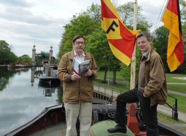 Fritz Wilhelm Achilles (l.) und Dr. Eckhard Schinkel präsentieren im Schiffshebewerk das neue Buch und haben dazu eine Original-Fahne der Reederei Fendel gehisst. Für sie war der Vater des Autors viele Jahre lang als Schiffsführer unterwegs.<br>Foto: LWL/Appelhans