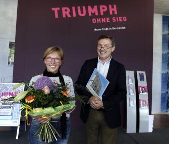 LWL-Museumsleiter Dr. Rudolf Aßkamp (r.) begrüßt Beatrix Guballa als 10.000. Besucherin der Ausstellung "Triumph ohne Sieg" mit einem Ausstellungskatalog und einem Blumenstrauß.<br>Foto: LWL/Wolter