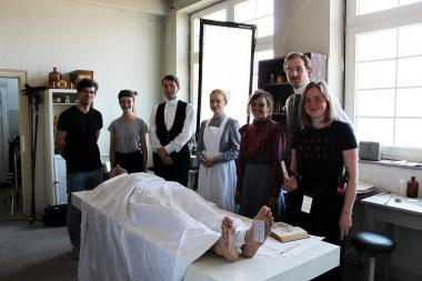 Gruppenbild mit Leiche (Julius Heeke) in der umgestalteten Gesundheitsstation des Textilwerks: Regisseur Mark Lorei (v.l.), Drehbuchautorin Cecilia Röski, die Schauspieler Fabian Nolte (Hausdiener), Lisa Sophie Laurent (Krankenschwester), Milena Straube (Louise von Kummerveldt), Wolf Danny Homann (Dr. Büchner) und Produktionsleiterin Lotte Ruf.<br>Foto: LWL
