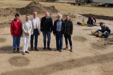 Stolz präsentieren (v.l.n.r.) LWL-Grabungstechnikerin Maria Hahne, LWL-Chefarchäologe Prof. Dr. Michael Rind, Bürgermeister Hans Hermann Bluhm, die LWL-Archäologen Dr. Sven Spiong und Dr. Hans-Otto Pollmann sowie Kerstin Schierhold vom LWL-Museum für Archäologie den im Boden anhand der dunklen Verfärbungen klar erkennbaren Hausgrundriss aus der Jungsteinzeit.<br>Foto: LWL/F. Kronfeld
