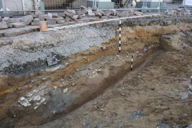 Archäologische Begleitarbeiten auf dem Beckumer Marktplatz. Im unteren Bereich des Baugrubenprofils ist eine Pflasterung aus Kalksteinbruchstücken zu sehen, die den Rest einer spätmittelalterlichen/frühneuzeitlichen Marktplatzoberfläche darstellt.<br>Foto: LWL/ A. Wunschel