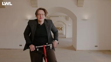 Museumsleiterin Dr. Sylvia Necker radelt durch die noch leeren Ausstellungsräume im LWL-Preußenmusum Minden. Video Still.<br>Foto: LWL