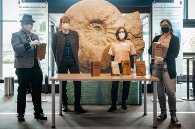 Der Museumsleiter Peter Fortner und der Bürgermeister Simon Hausstetter übergeben die Holzbücher an die Ausstellungsmacherinnen Lisa Klepfer und Nadine Howe des LWL-Museums für Naturkunde (v.l.n.r.).<br> Foto: LWL/Steinweg