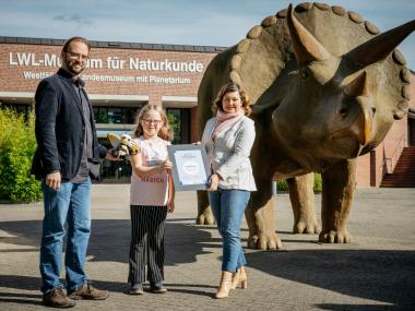 Kim Spiekermann (8 Jahre) aus Ostbevern hat den Schüler:innen-Wettbewerb &quot;Arten-Olympiade&quot; des LWL-Museums für Naturkunde und der Stiftung Münster der Sparda-Bank West gewonnen. Museumsdirektor Dr. Jan Ole Kriegs (li.) übergab zusammen mit Ute Cewe, Geschäftsführerin der Sparda Stiftung, die Urkunde.&lt;br&gt;Foto: LWL/Steinweg 