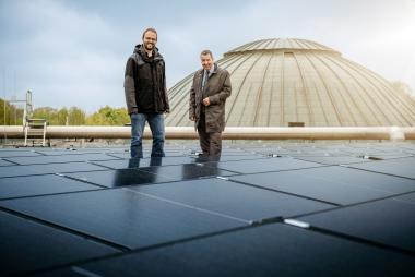 Matthias Gundler (re.), Betriebsleiter des LWL-Bau- und Liegenschaftsbetriebes und Museumsdirektor Dr. Jan Ole Kriegs besichtigen die fertiggestellte Photovoltaikanlage auf dem Dach des LWL-Museums für Naturkunde. Im Hintergrund ist die Kuppel des Planetariums zu sehen.<br>Foto: LWL/Steinweg