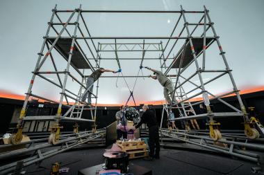 Ein Mitarbeiter der Firmen "GOTO" (Hersteller des Sternprojektors) und "Skypoint" (Software-Steuerung des Sternprojektors) sowie zwei Mitarbeiter des Planetariums setzen mittels der Hebe-Konstruktion den neuen Sternenprojektor Orpheus im Planetarium des LWL-Museums für Naturkunde in seine endgültige Position.<br>Foto: LWL/Steinweg