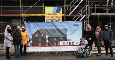 Vera Herbst, Einrichtungsleitung des LWL-Wohnverbundes Kreis Steinfurt (3.v.l.) befestigte mit Mitarbeitenden und zukünftigen Bewohner:innen sowie Marion Konermann vom Personalrat (l.) ein Banner mit Informationen zum Neubau am Bauzaun.<br>Foto: LWL/Westerkamp
