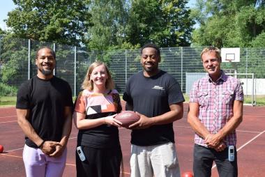 Ballübergabe auf dem Sportplatz: (v.l.) Trainer Mike Davis, Bianka Müller, Lehrerin der LWL-Schule im Heithof, Phillip Gamble sowie Lehrer Stefan Saggel.<br>Foto: LWL